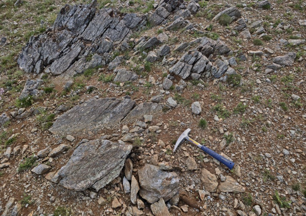 Resistant silicified ribs across a weathered slope, hammer for scale